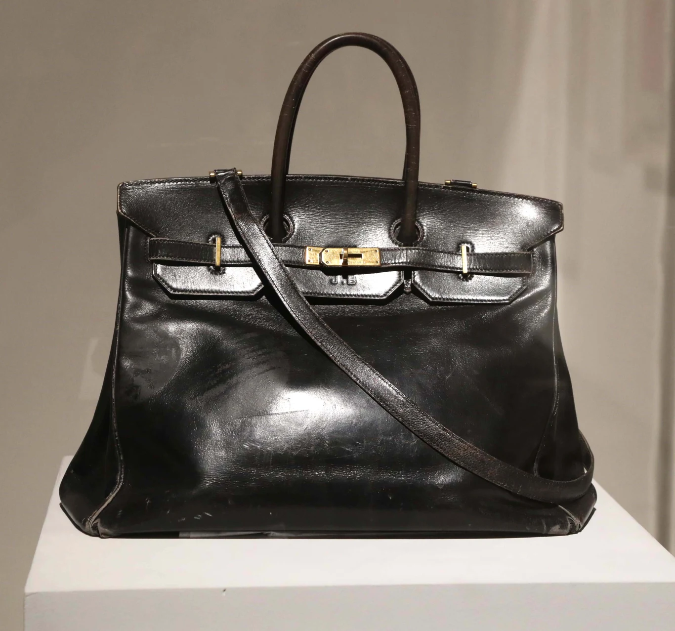 Czarna, skórzana torebka z krótkimi uchwytami oraz długim paskiem na ramię, ozdobiona złotym zapięciem na środku.