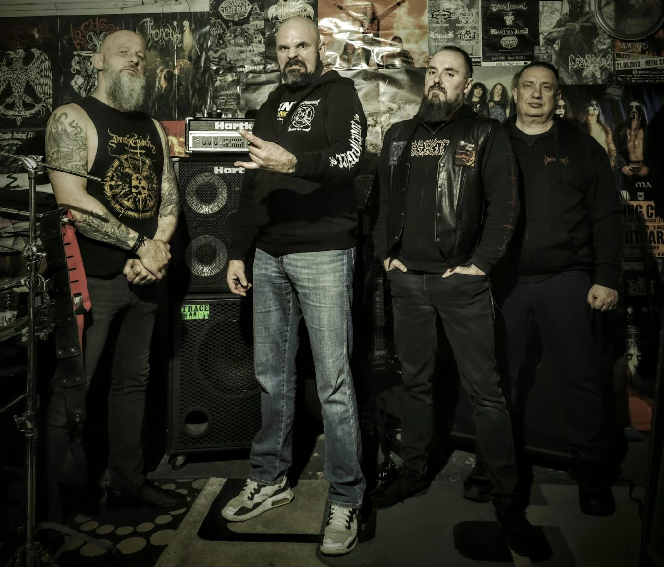 Hell-Born odlicza do premiery Czterech członków Hell-Born pozuje przy sprzęcie muzycznym na tle ściany z plakatami rockowymi.