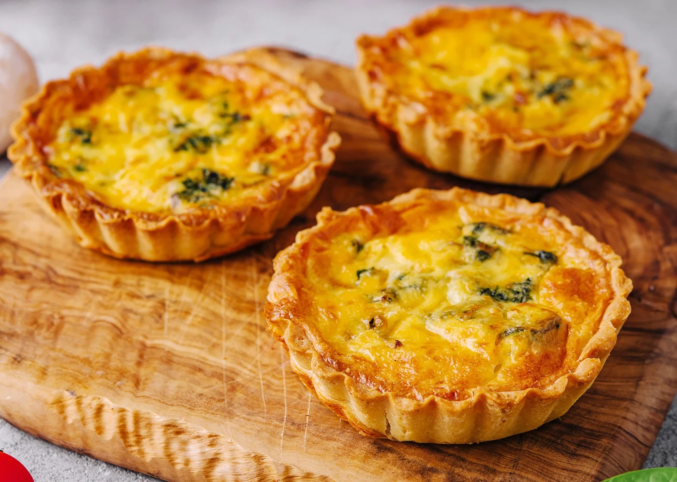 Dania, które zawsze sprawdzą się w komunijnym menu Trzy mini tarty z farszem jajecznym i ziołami na drewnianej desce, propozycja na menu komunijne.