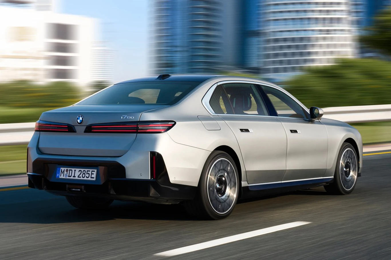 BMW serii 7 srebrny sedan BMW serii 7 jedzie po wielopasmowej drodze w miejskiej scenerii, na tle nowoczesnych wieżowców i rozmytego tła