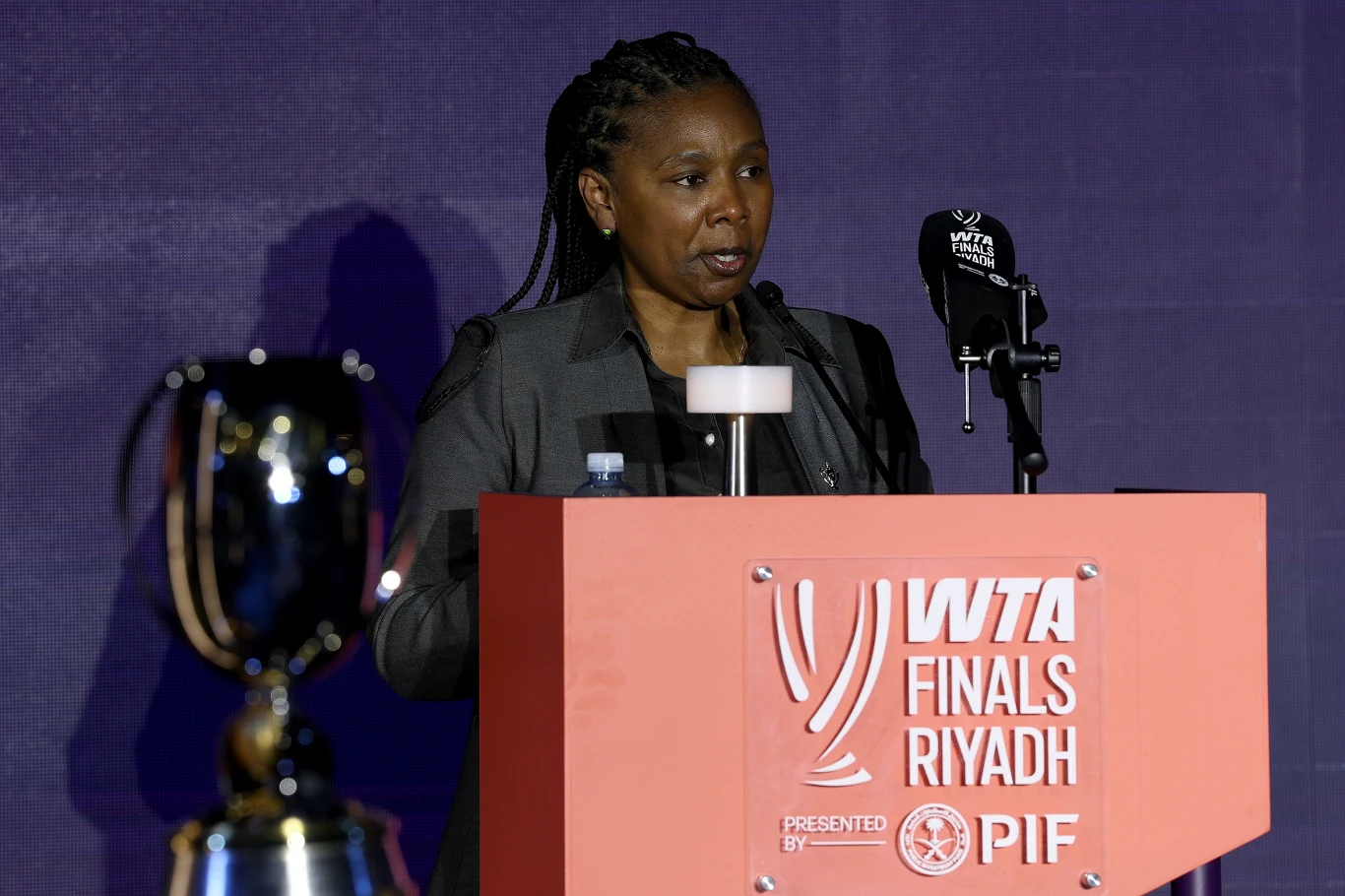 Portia Archer Portia Archer przemawia przy podium z logo WTA Finals Riyadh, obok stoi puchar, tło fioletowa ściana