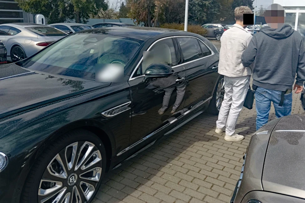 23-latek został zatrzymany podczas próby odebrania Bentley'a wartego 2 mln zł Czarny Bentley o wartości 2 mln zł zaparkowany na kostce, obok dwóch mężczyzn rozmawiających na parkingu