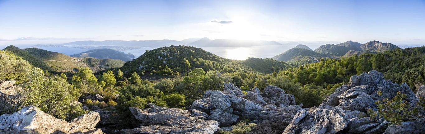 panorama skalistych wzgórz porośniętych gęstą zielenią, w oddali rozlewające się morze i wyłaniające się z niego kolejne pasma górskie oświetlone łagodnym światłem słonecznym