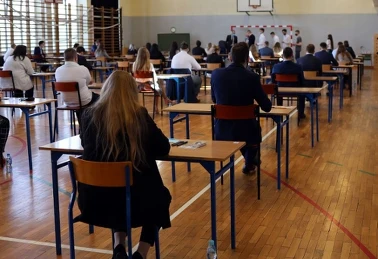 Maturzystka w białej koszuli siedzi w sali egzaminacyjnej — długopis, arkusz, butelka wody i banan na ławce