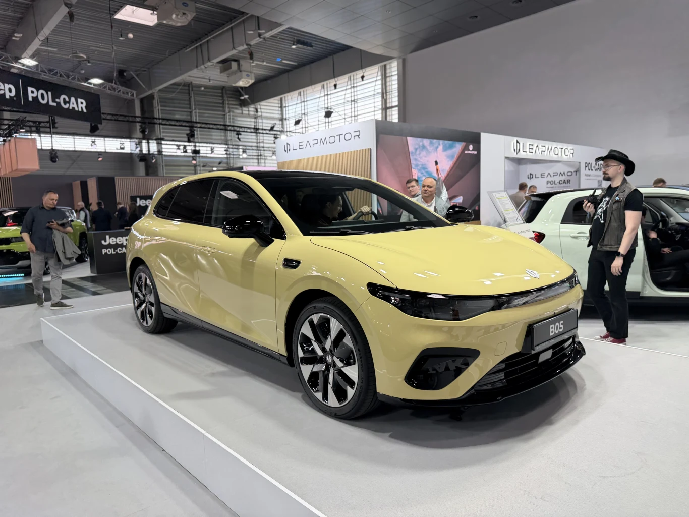 żółty samochód elektryczny Leapmotor B05 ustawiony na podwyższeniu podczas targów motoryzacyjnych, wokół pojazdu stoją zwiedzający, a w tle widoczne są stoiska innych marek motoryzacyjnych