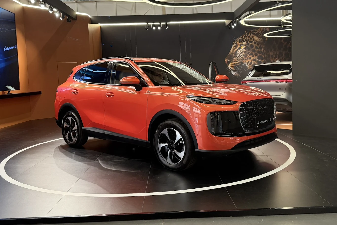 Lepas L6 Lepas L6, czerwony SUV na podświetlonej platformie; w tle lampart i fragment drugiego auta