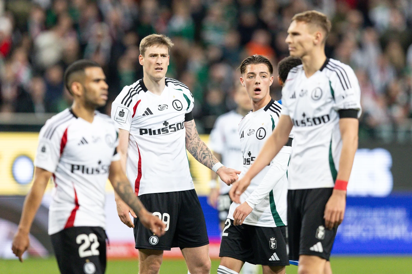 Legia Warszawa Czterech piłkarzy Legii Warszawa w białych koszulkach stoi na boisku podczas meczu.