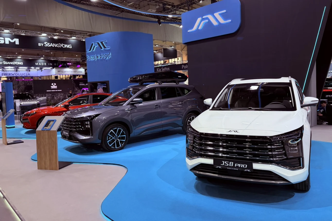 Gama modeli osobowy JAC. Na pierwszym planie JS8 Pro Trzy SUV-y JAC na ekspozycji targowej, na przodzie biały JS8 Pro, w tle firmowe logotypy.