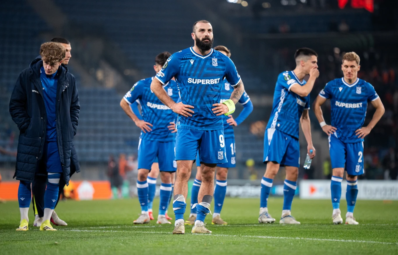 Lech Poznań kolejną polską drużyną ukaraną przez UEFA Piłkarze Lecha Poznań w niebieskich strojach stoją na murawie stadionu, kapitan w centrum grupy.