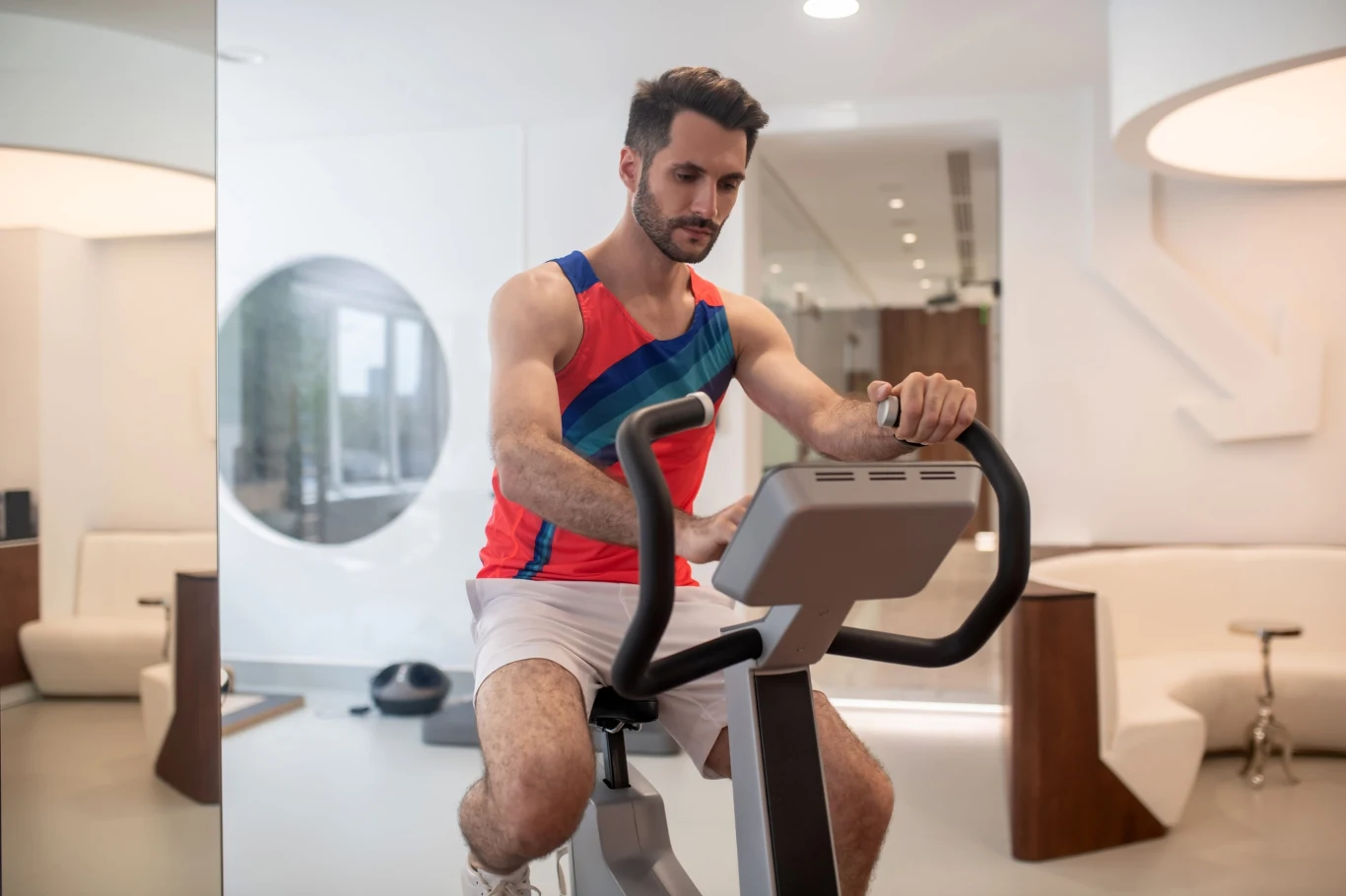 mężczyzna w sportowym stroju intensywnie ćwiczy na rowerze stacjonarnym w nowoczesnej, jasnej siłowni