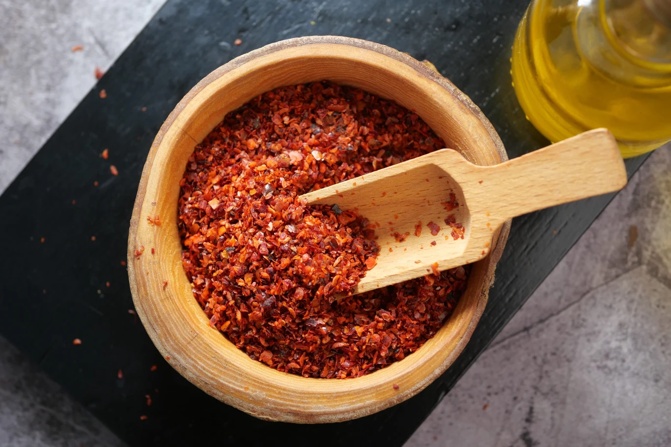Szczypta chili dziennie pomoże na objawy zespołu metabolicznego. Ma też moc łagodzenia bólu Drewniana miska wypełniona grubą mieszanką papryki chili, obok mała drewniana łopatka, na drugim planie szklana butelka z oliwą.