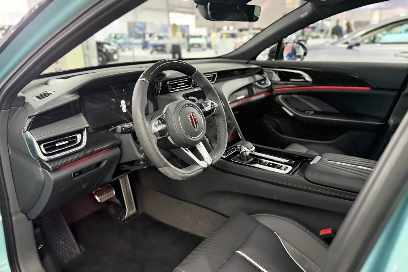 Hongqi H6 nowoczesne wnętrze samochodu z cyfrowym panelem wskaźników, wielofunkcyjną kierownicą, środkową konsolą z elektroniczną dźwignią zmiany biegów oraz czarną tapicerką ozdobioną czerwonymi akcentami
