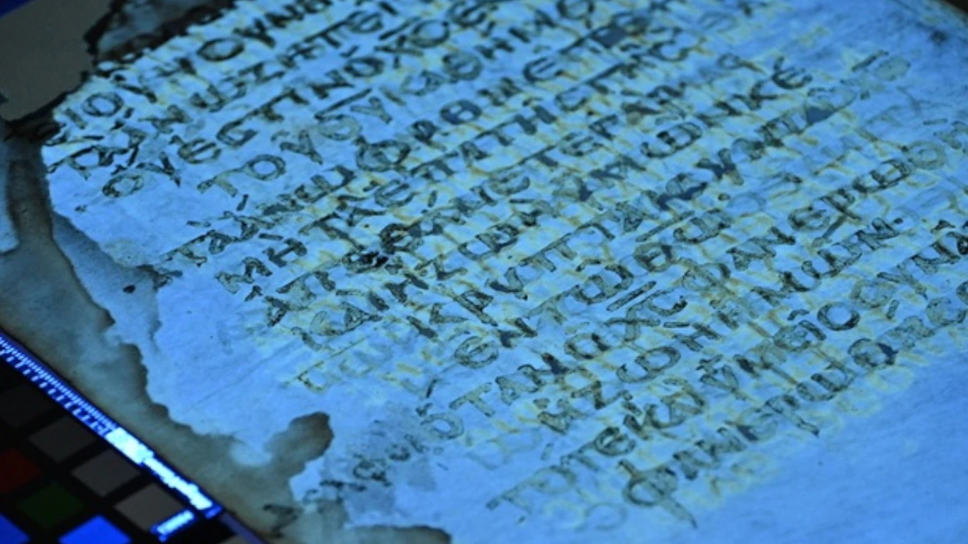 Archeolodzy odkryli zaginiony manuskrypt z nieznanymi fragmentami Nowego Testamentu Fragment historycznego tekstu w dawnym języku; zniszczony papier oświetlany niebieskim światłem