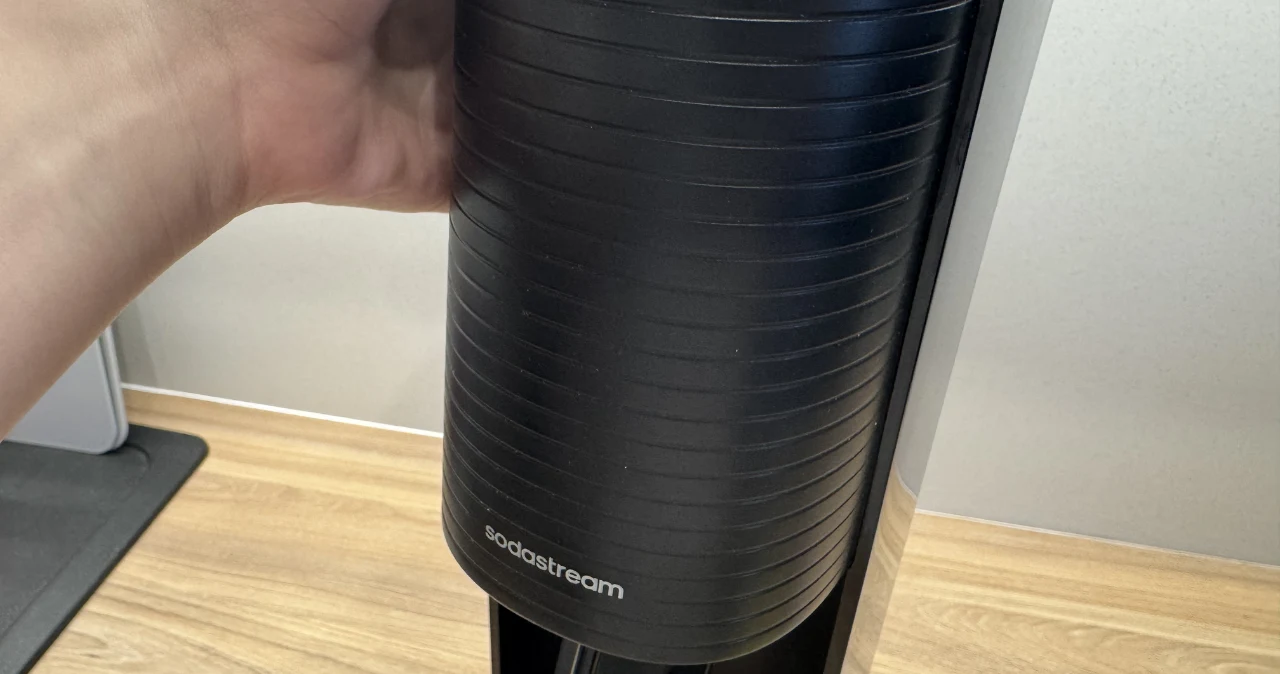 Lidl odpalił SodaStream, a Biedronka odpowiada – ten sprzęt jest tańszy i robi się ciekawie Czarny saturator SodaStream trzymany przez rękę na drewnianym blacie kuchennym.
