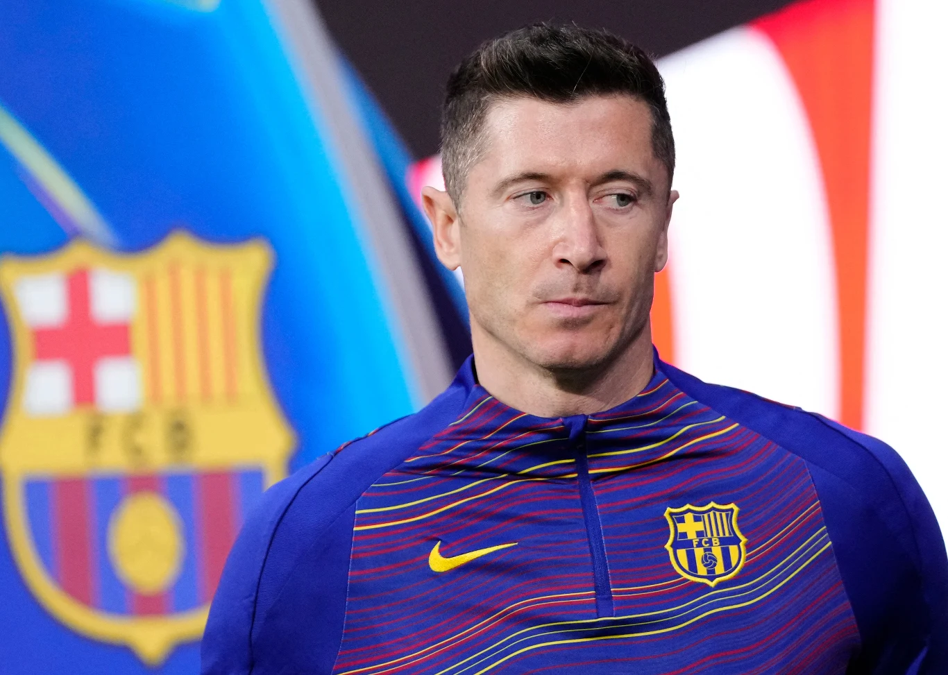 piłkarz w stroju FC Barcelona stoi na tle dużego, rozmytego herbu klubu