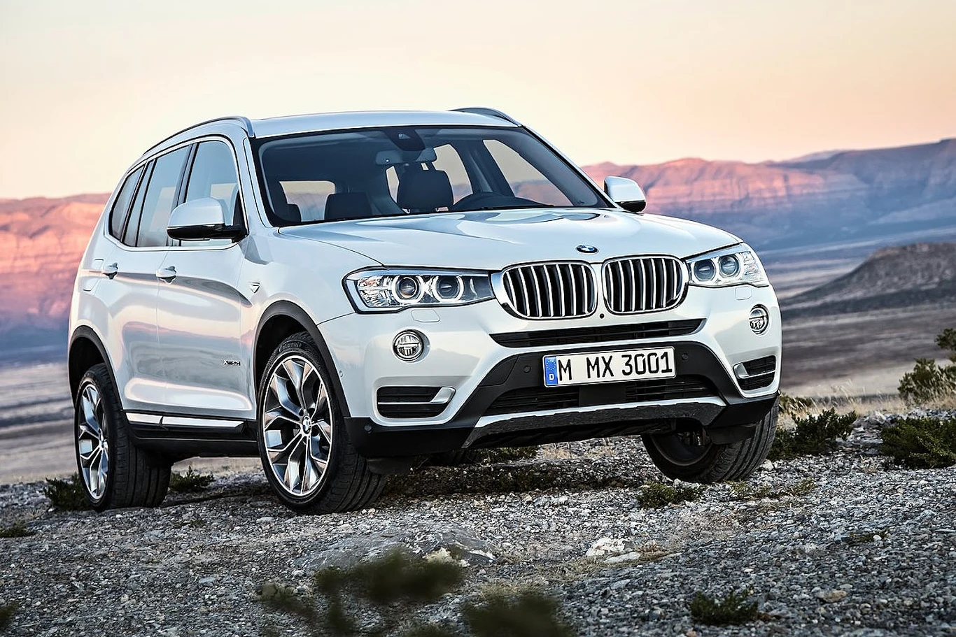 BMW X3 z rocznika 2015 biały SUV marki BMW zaparkowany na kamienistej drodze na tle pustynnego krajobrazu i gór w oddali, auto ma charakterystyczny grill, masywne reflektory oraz aluminiowe felgi