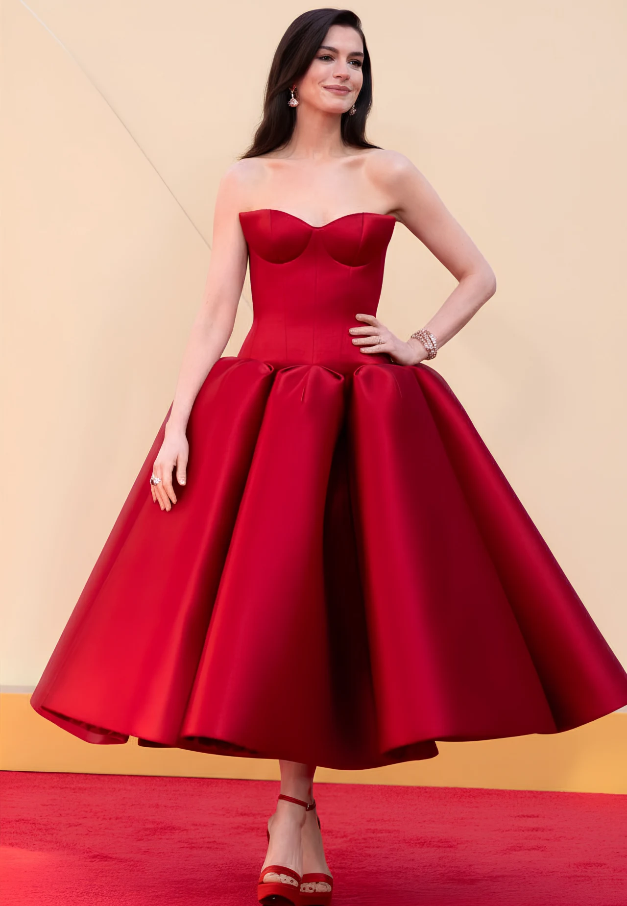 kobieta w eleganckiej, rozkloszowanej sukni w intensywnie czerwonym kolorze, na czerwonym dywanie, z rozpuszczonymi włosami i delikatną biżuterią