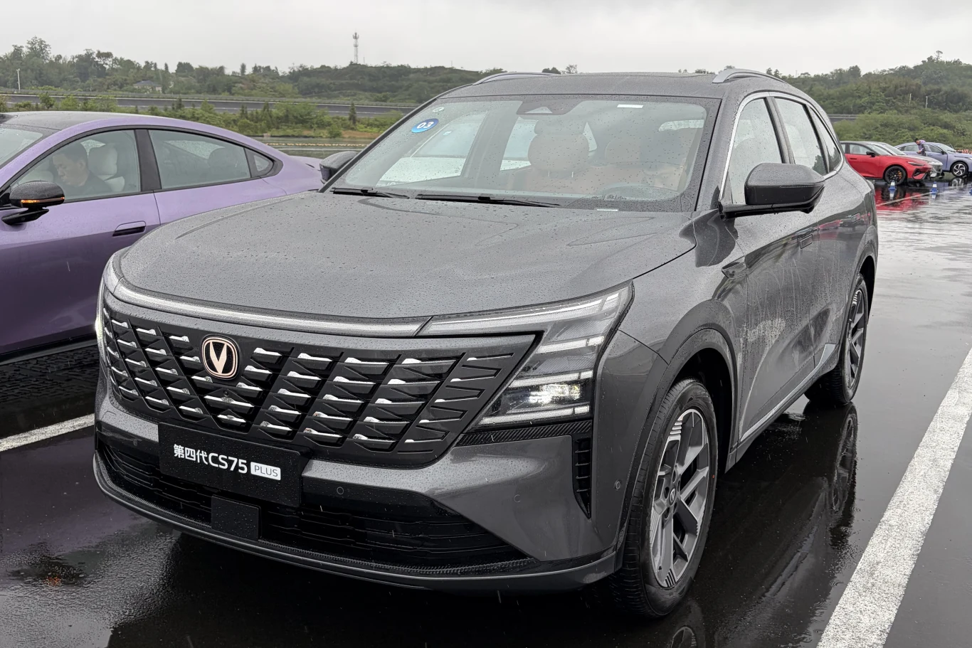 Changan CS75 PLUS należy do segmentu D i celuje w potrzeby rodzin. szary nowoczesny SUV marki Changan z charakterystycznym dużym, czarnym grillem i smukłymi reflektorami LED, ustawiony na mokrym asfalcie parkingu