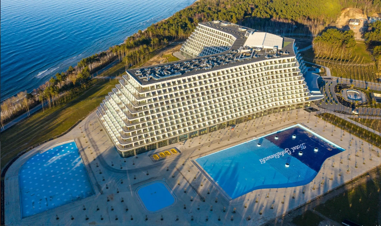 Hotel Gołębiewski Hotel Gołębiewski w Pobierowie, wielopiętrowy budynek tarasowy nad morzem, z basenami i otaczającą zielenią.