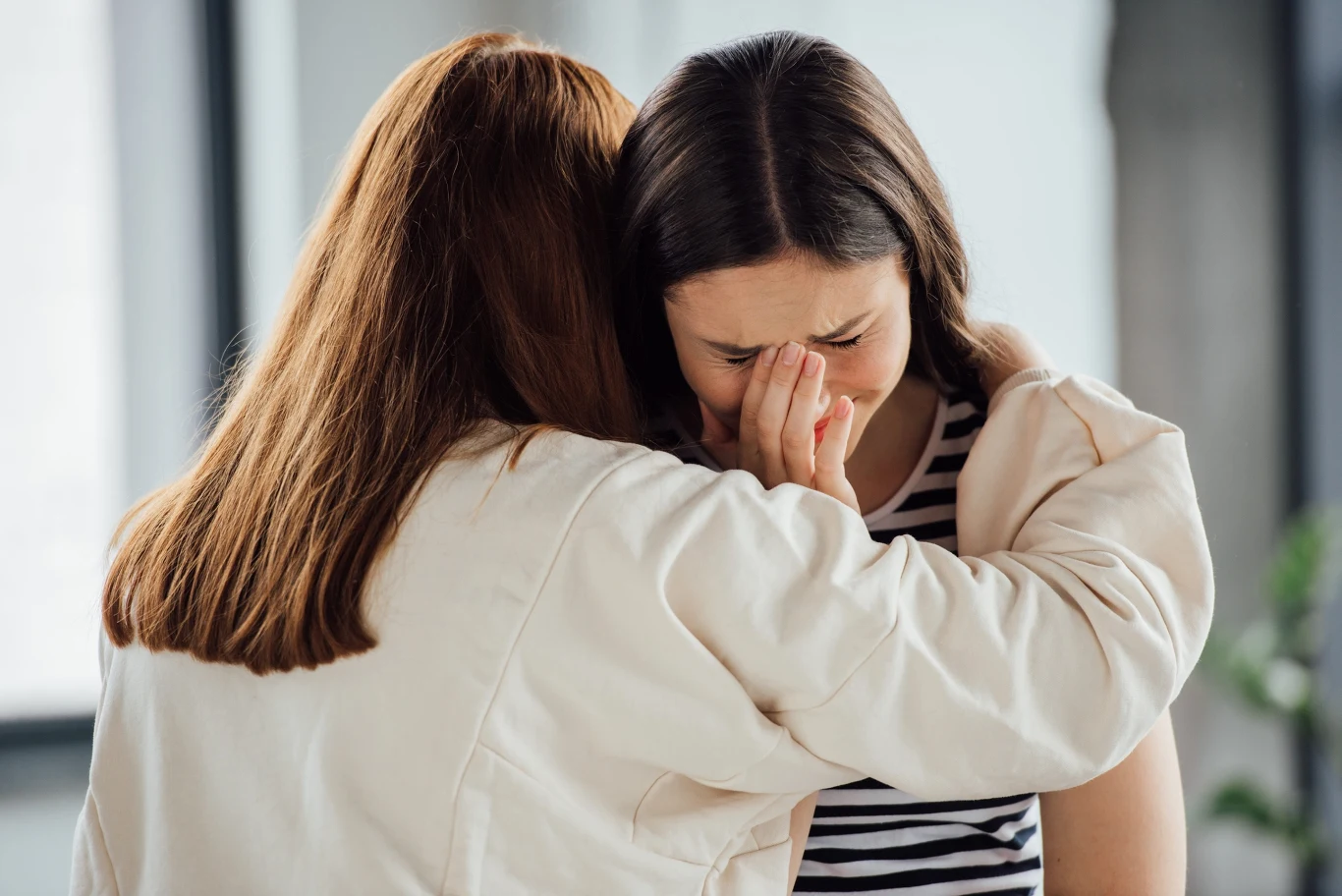 dwie kobiety obejmujące się, jedna z nich płacze i zasłania twarz dłonią, druga pociesza ją serdecznym uściskiem