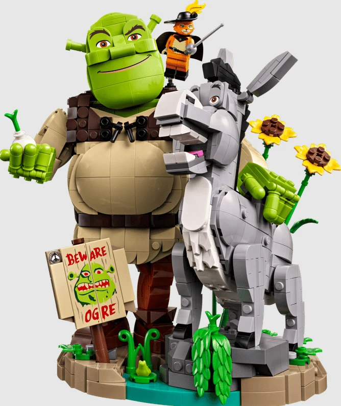 Shrek, Osioł i Kot w butach (72423) postacie Shrek, Osioł i Kot w Butach zbudowane z klocków LEGO, otoczone kwiatami słonecznika, z ręcznie wykonanym znakiem ostrzegającym przed ogrem