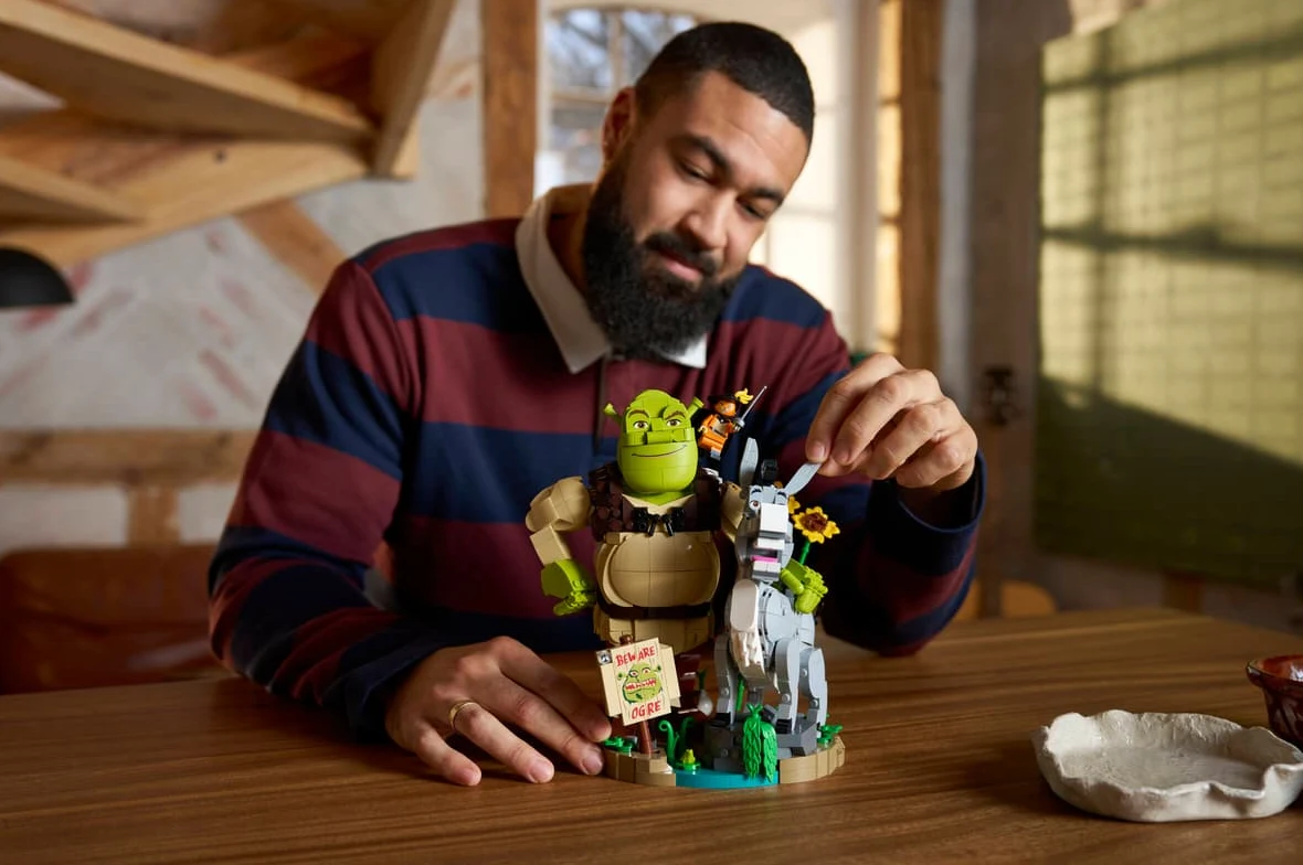 Shrek, Osioł i Kot w butach (72423) mężczyzna siedzi przy stole i układa zestaw klocków przedstawiający figurki Shreka oraz Osła, skupiając się na detalach budowli