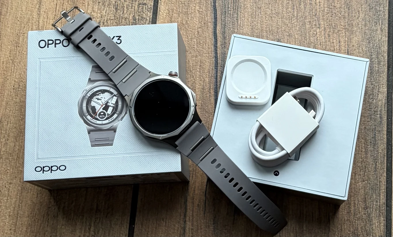 Zawartość opakowania z Oppo Watch X3. smartwatch OPPO z szarym paskiem położony na oryginalnym pudełku, obok otwarte opakowanie z ładowarką i kablem USB, całość na drewnianym blacie