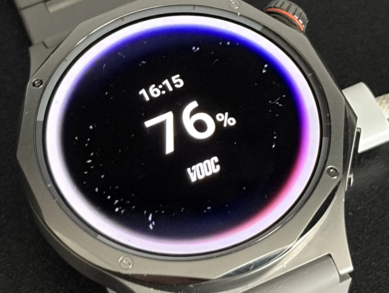 Ładowanie Oppo Watch X3 od 0 do 100 proc. trwa około 75 minut. nowoczesny smartwatch z okrągłym wyświetlaczem pokazujący godzinę 16:15, poziom naładowania baterii 76% oraz z białym paskiem