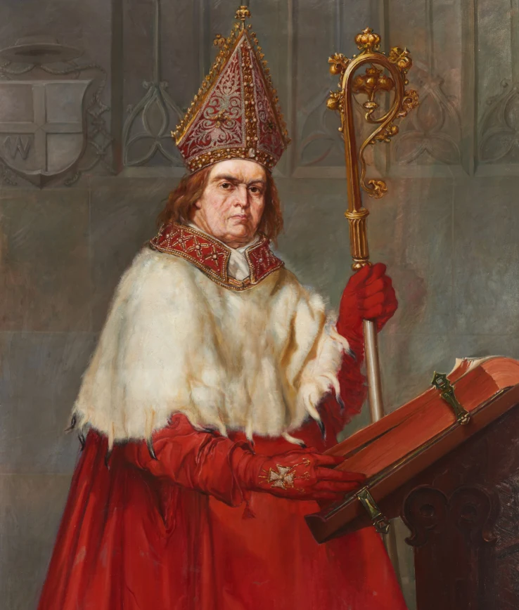mężczyzna w stroju biskupa z ozdobnym pastorałem w prawej dłoni, ubrany w czerwoną szatę i białą pelerynę, stoi przed otwartą księgą na pulpicie, na głowie nosi bogato zdobioną infułę