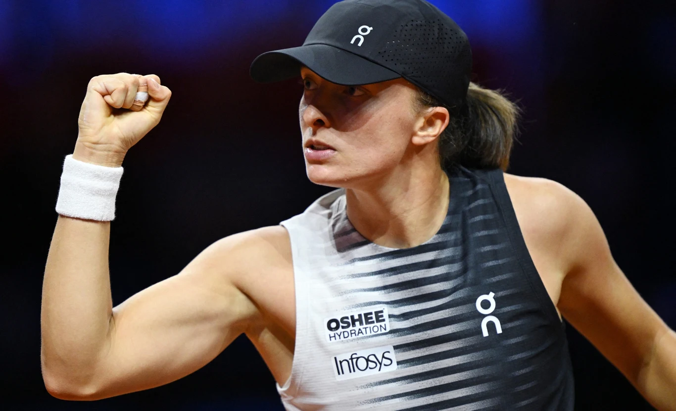 Iga Świątek Iga Świątek w sportowym stroju i czapce pokazuje zaciśniętą pięść podczas meczu tenisowego.