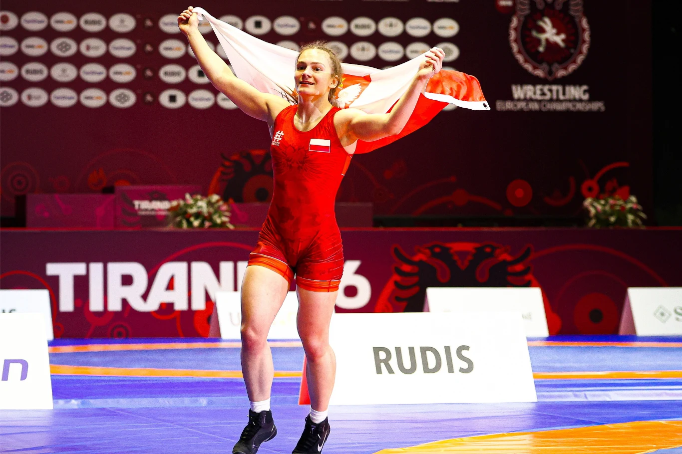 Magdalena Głodek-Liszewska Magdalena Głodek-Liszewska w czerwonym stroju z biało-czerwoną flagą na macie podczas mistrzostw Europy w zapasach w Tiranie.