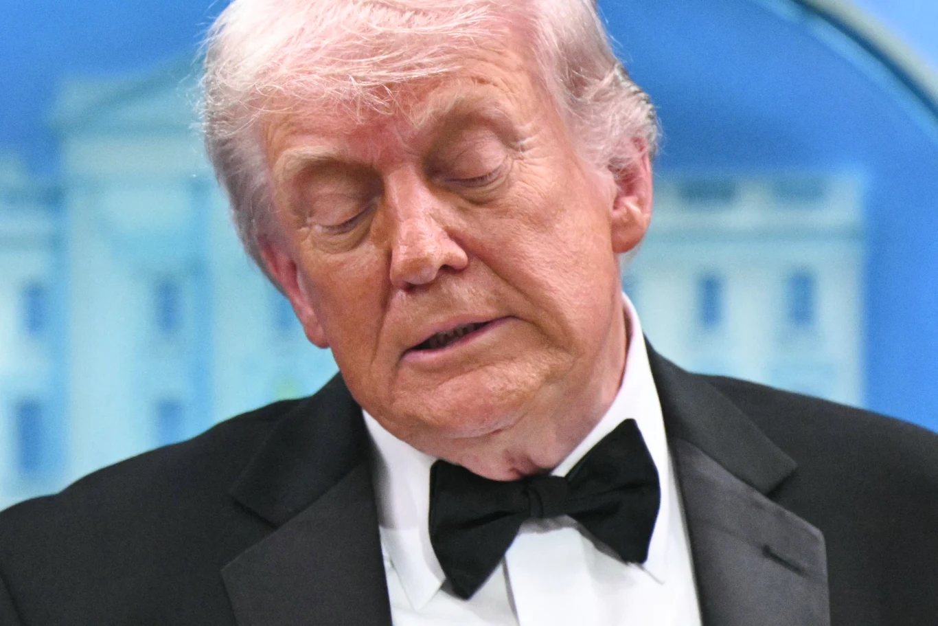 Donald Trump Donald Trump w smokingu i muszce, z zamkniętymi oczami, na tle białego budynku z kolumnami.
