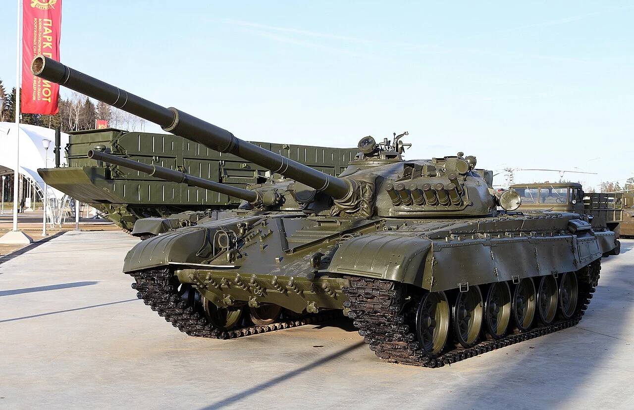 Rosja modernizuje 800 czołgów T-72A do wersji T-72B3M Czołg T-72A w zielonym kamuflażu z długą lufą, na utwardzonej powierzchni, w tle pojazd wojskowy.