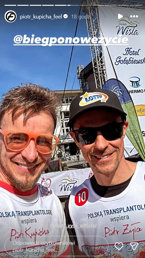 dwóch uśmiechniętych mężczyzn w sportowych koszulkach z napisem 'Polska Transplantologia wspiera', jeden z nich ma pomarańczowe okulary, a drugi czapkę z daszkiem i okulary przeciwsłoneczne; w tle widoczne są elementy sceny plenerowej oraz banery spons...