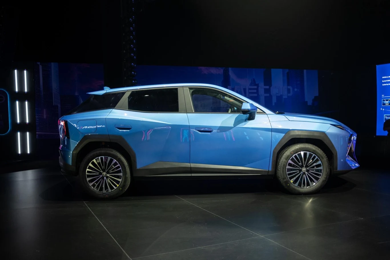 nowoczesny, niebieski SUV o ostrych liniach nadwozia, charakterystycznych felgach i wyrazistych kształtach reflektorów, ustawiony w jasnym świetle na tle ciemnego otoczenia