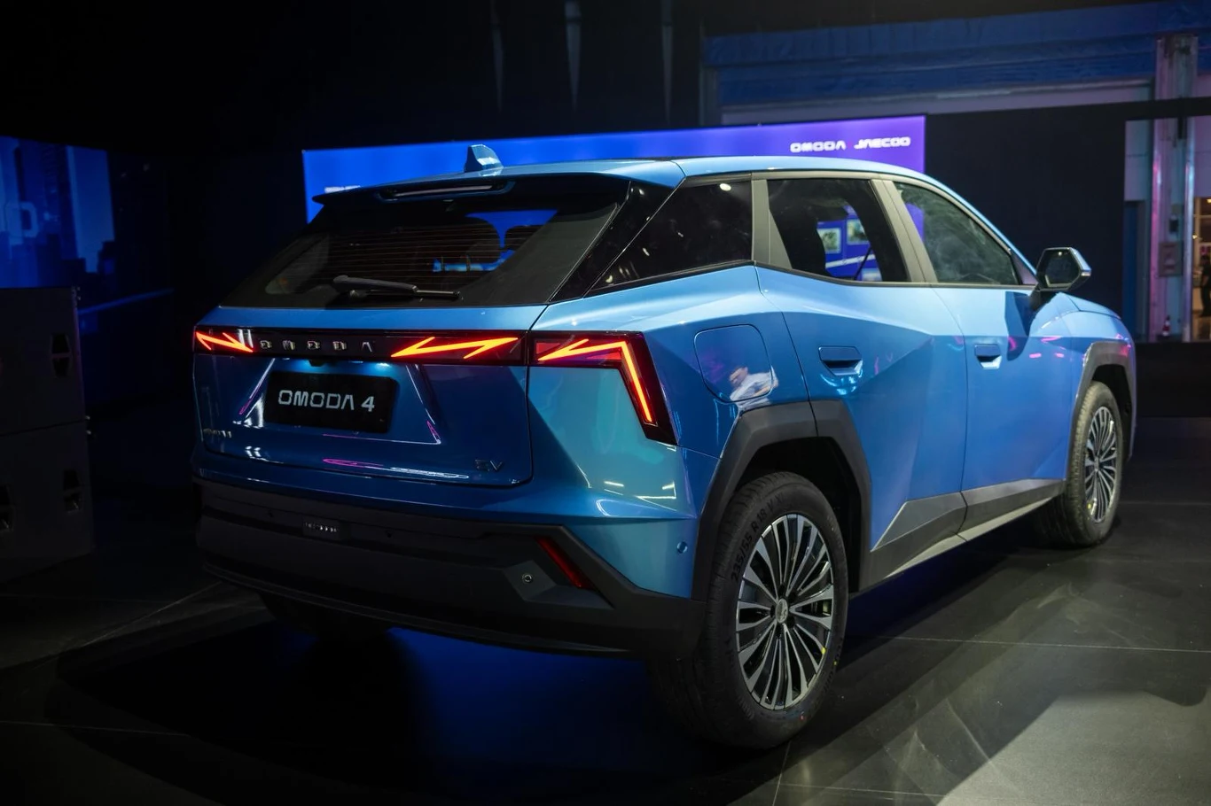 niebieski nowoczesny SUV Omoda 4 z charakterystycznymi, ostrymi liniami nadwozia oraz wyrazistym, geometrycznym wzorem świateł tylnych, ustawiony na czarnym tle w dobrze oświetlonym studio