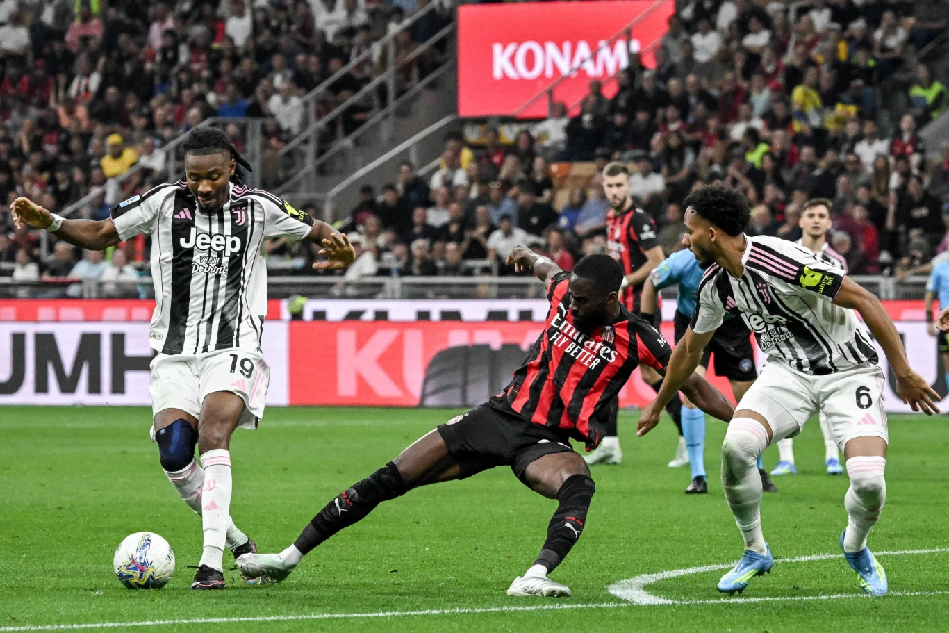Khephren Thuram (pierwszy z lewej) trafił do bramki Milan, ale uderzał z pozycji spalonej zacięta walka o piłkę między zawodnikiem w czarno-czerwonej koszulce a dwoma piłkarzami w biało-czarnych strojach na tle wypełnionych trybun stadionu, dynamiczne ruchy i napięcie sytuacji podkreślają intensywność meczu