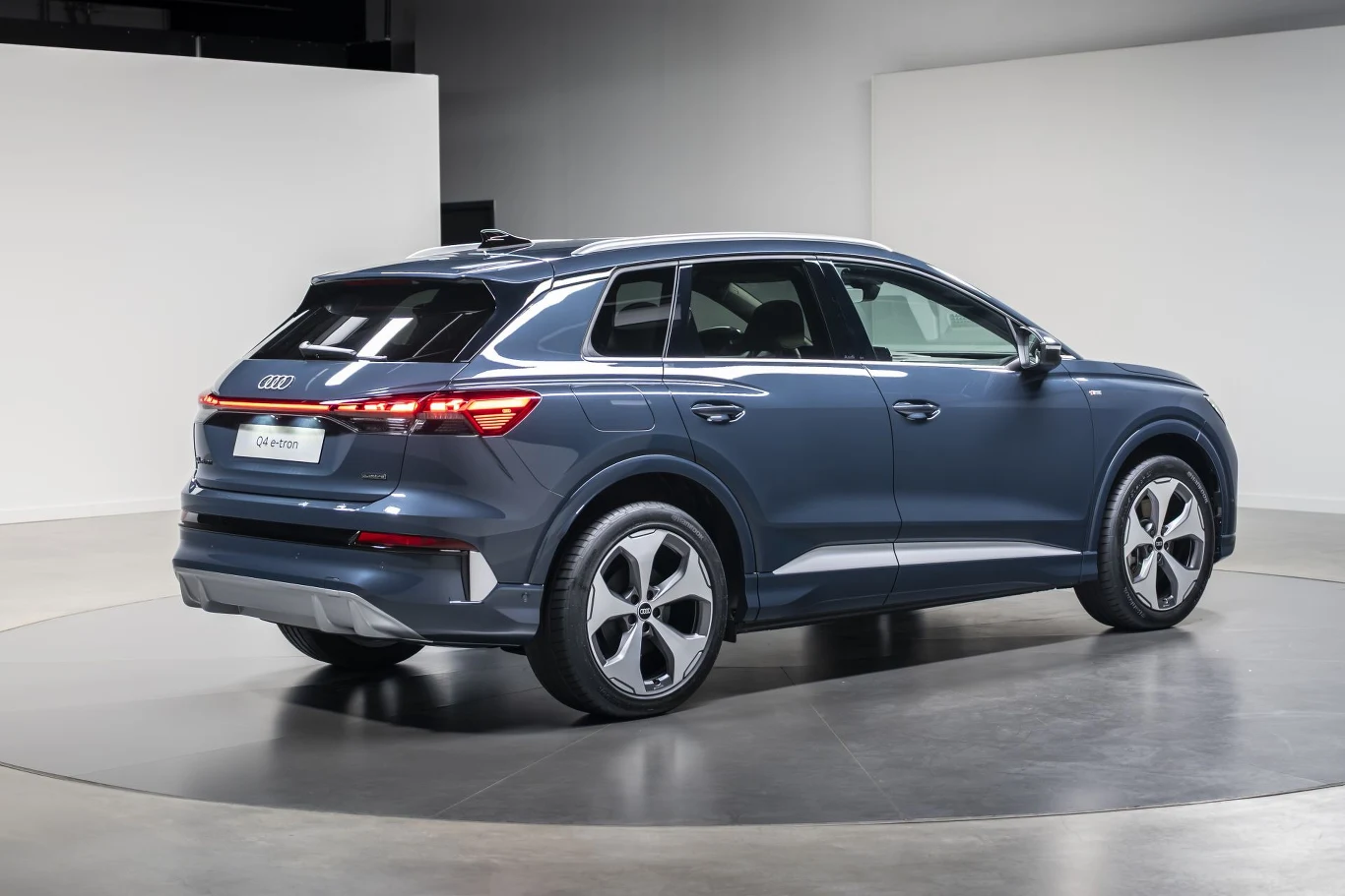 Granatowy SUV Audi z nowoczesnymi, aerodynamicznymi felgami stoi na obrotowej platformie w minimalistycznym, jasnym wnętrzu.