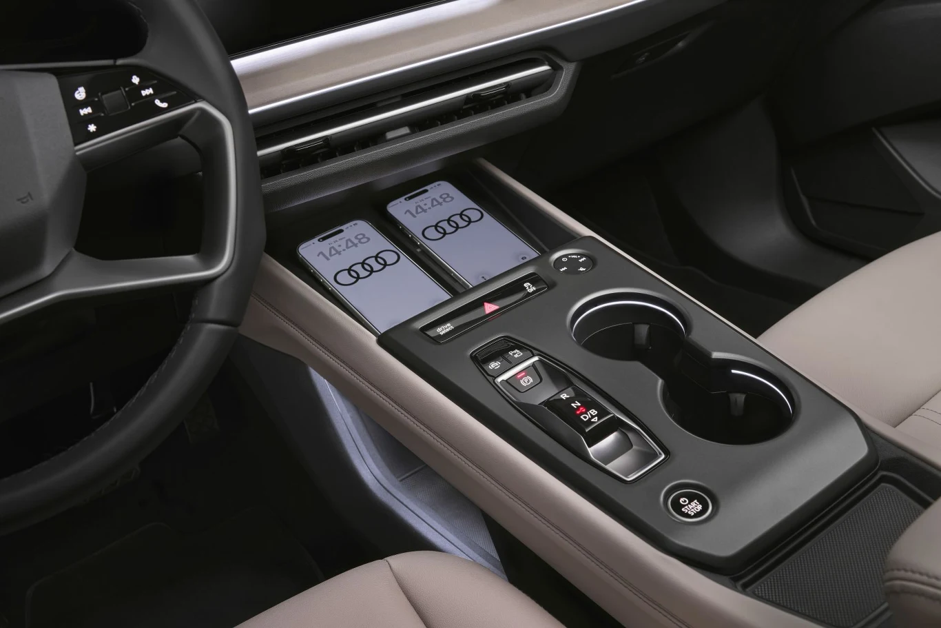konsola środkowa nowoczesnego samochodu marki Audi z dwoma bezprzewodowymi ładowarkami na smartfony, designerską dźwignią zmiany biegów, przyciskami funkcyjnymi oraz podwójnym uchwytem na kubki