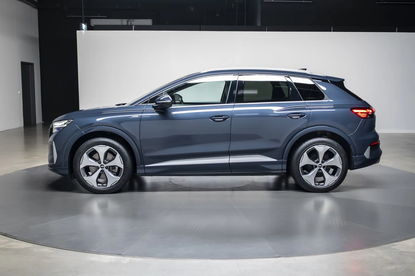 ciemnoniebieski SUV klasy premium ustawiony bokiem na obrotowej platformie w minimalistycznym, dobrze oświetlonym wnętrzu; samochód wyróżnia się nowoczesnym designem, charakterystycznymi felgami i chromowanymi elementami wykończenia