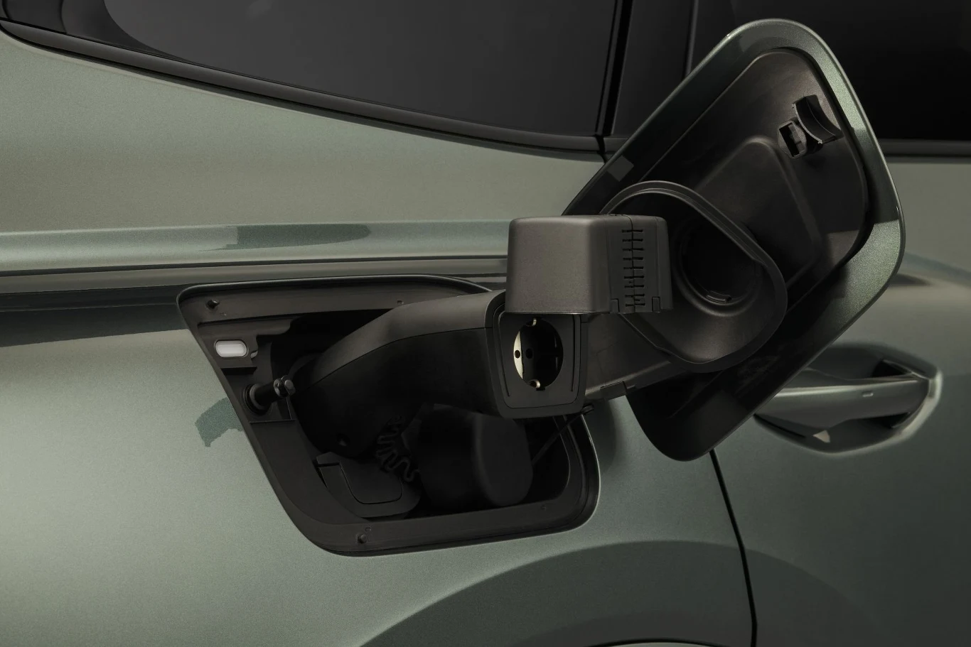 wtyczka ładowania samochodu elektrycznego podłączona do gniazda ładowania zamontowanego w nadwoziu auta o metalicznej, jasnej karoserii