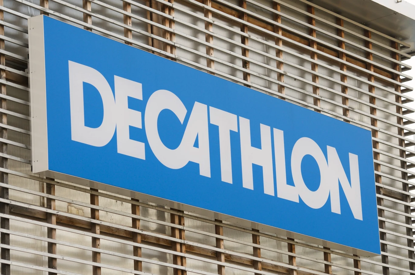 Decathlon wzywa do zwrotu wadliwego produktu Niebieski szyld z białym napisem DECATHLON na tle jasnej elewacji z metalowymi listwami.