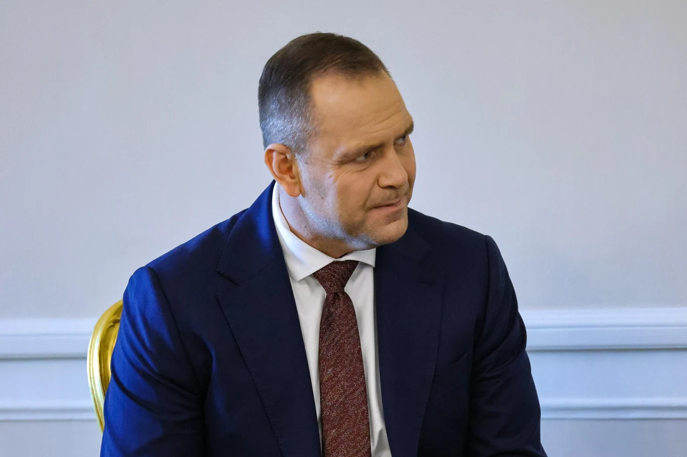 Prezydent Karol Nawrocki Prezydent Karol Nawrocki w granatowym garniturze i bordowym krawacie siedzi na żółtym krześle na tle jasnej ściany