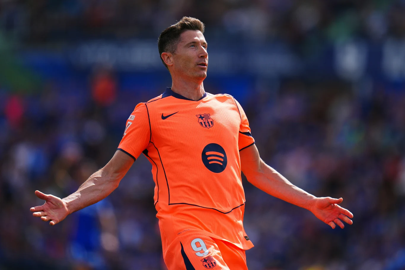 Robert Lewandowski Robert Lewandowski w pomarańczowym stroju FC Barcelony z numerem 9 podczas meczu, rozkłada ręce na boisku.