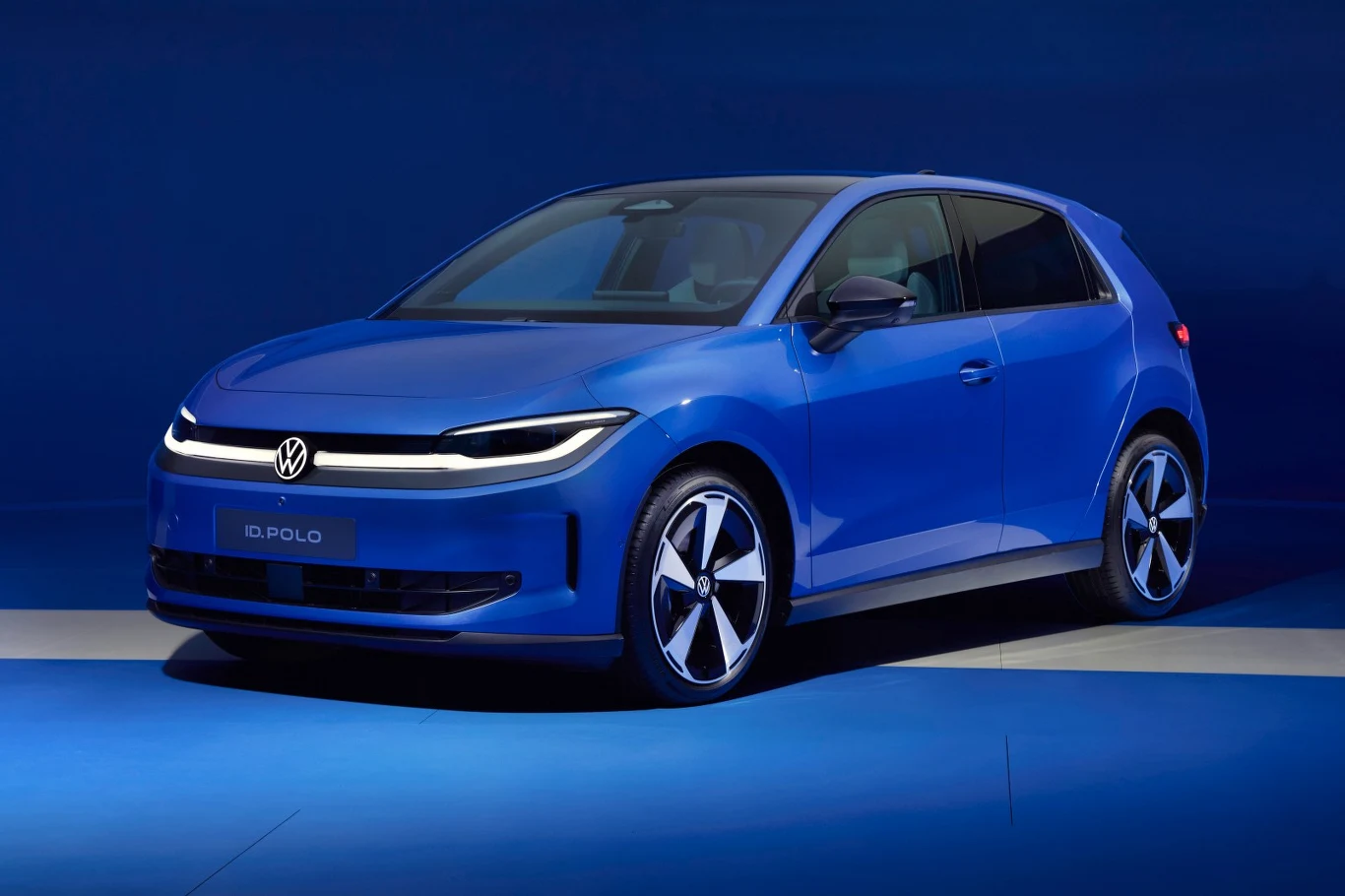 Od razu widać, że to Polo. Tak samo mogłaby wyglądać wersja spalinowa niebieski samochód osobowy marki Volkswagen z nowoczesnym, aerodynamicznym nadwoziem, charakterystycznymi reflektorami LED i eleganckimi felgami na tle jednolitego, niebieskiego studia