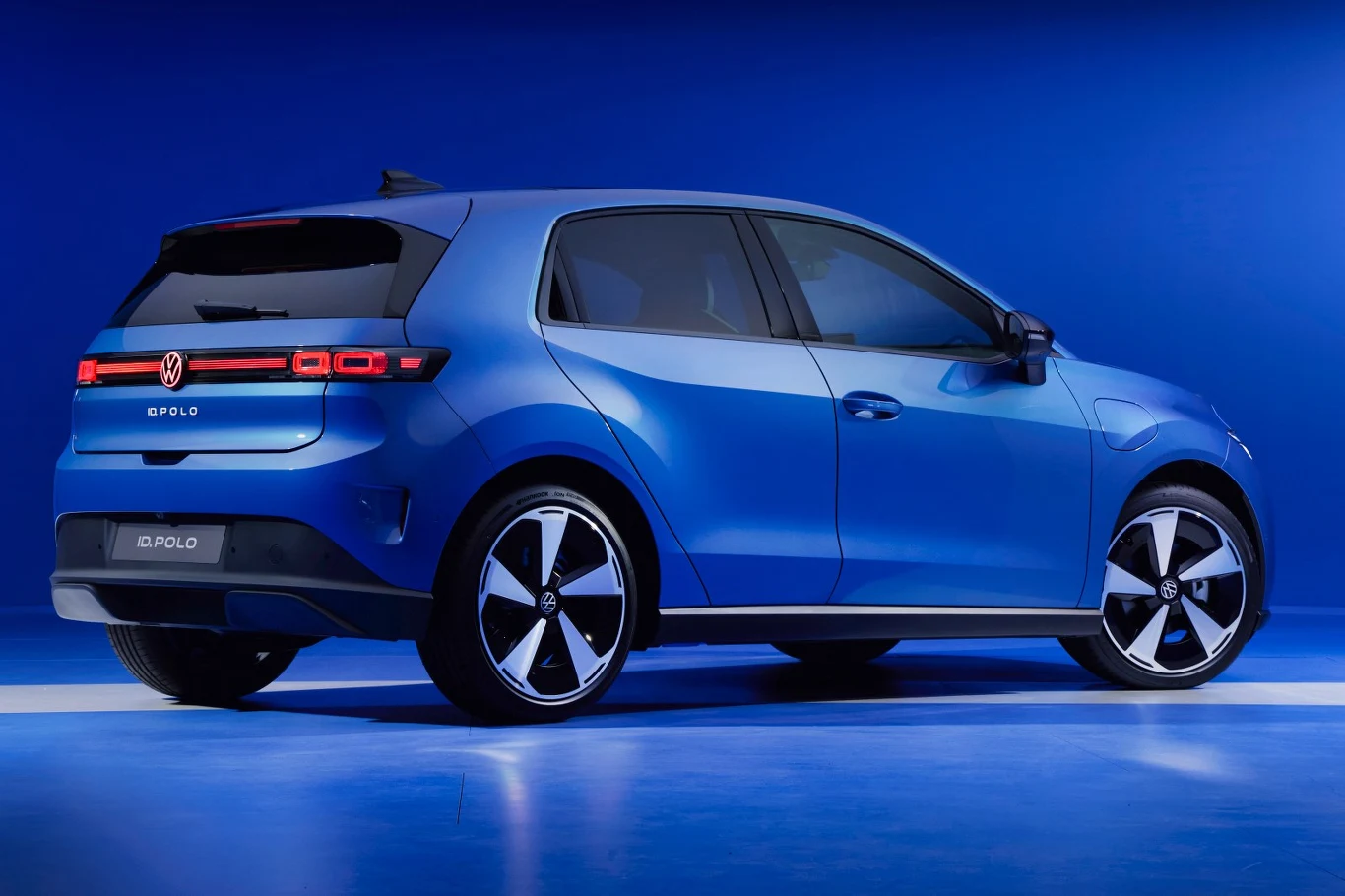 W żadnej wersji nie przewidziano elektrycznie otwieranej pokrywy bagażnika niebieski samochód Volkswagen Polo w nowoczesnej stylistyce, ustawiony na jasnym tle, z wyraźnie widocznymi tylnymi światłami LED i dużymi, czarno-srebrnymi felgami