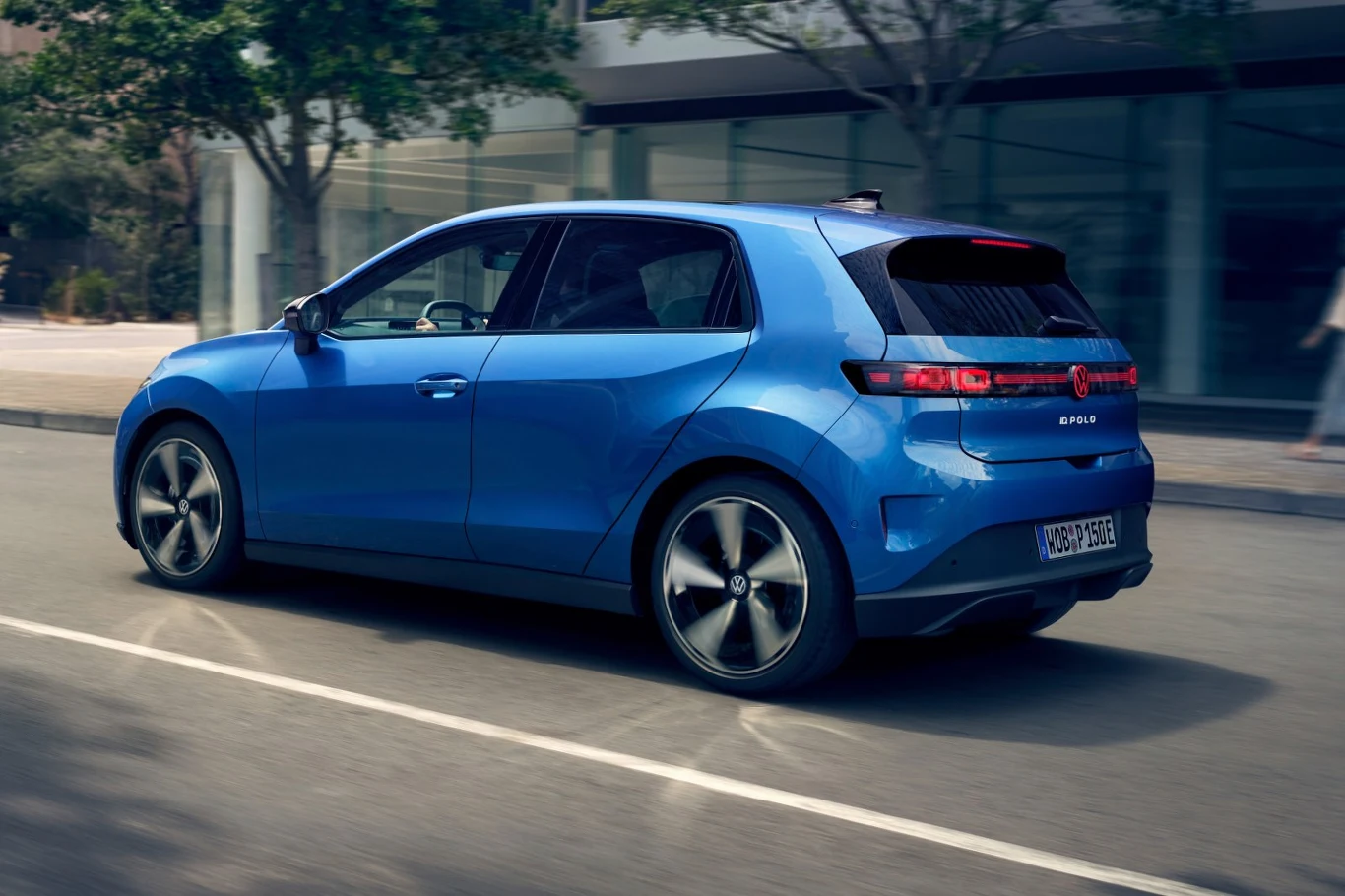 Z najmniejszą baterią elektryczne Polo przejedzie do 329 KM na jednym ładowaniu niebieski samochód osobowy o nowoczesnym designie i dynamicznej sylwetce poruszający się po ulicy miejskiej, otoczony szklanymi budynkami i drzewami