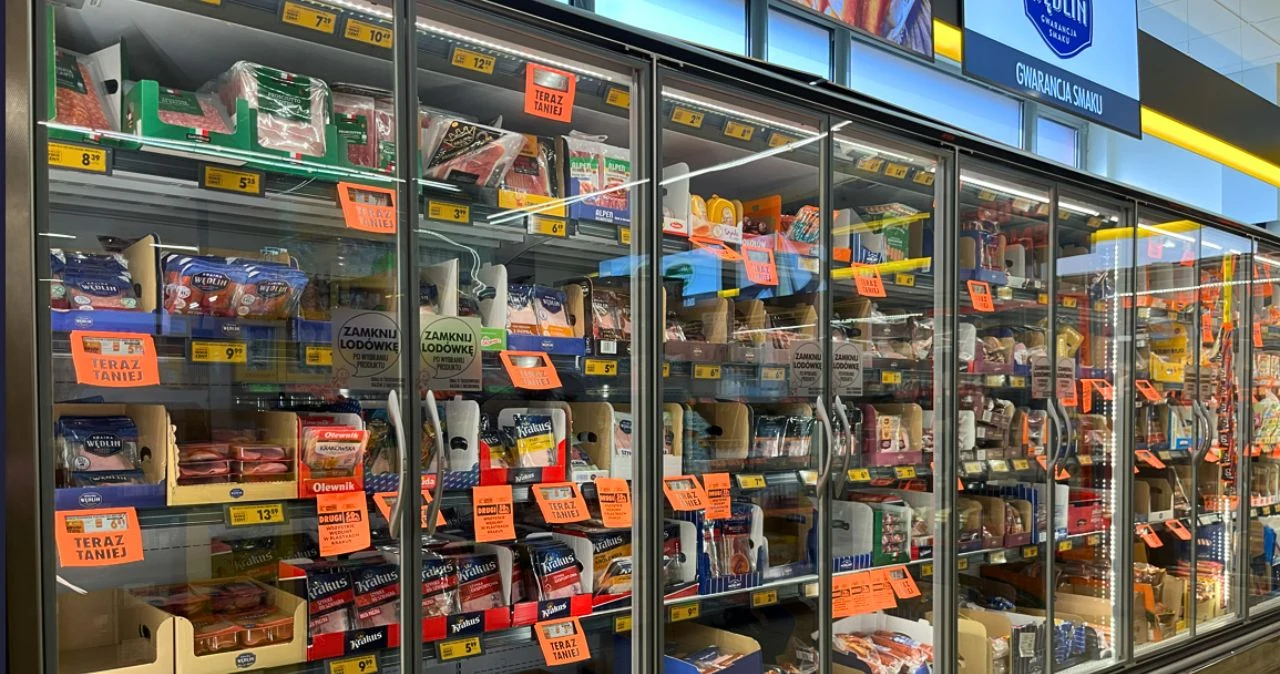 Biedronka ruszyła z majówką. Grill i gratisy przyciągają klientów Chłodziarki w Biedronce z paczkowanym mięsem i wędlinami, widoczne pomarańczowe etykiety promocyjne na drzwiach.