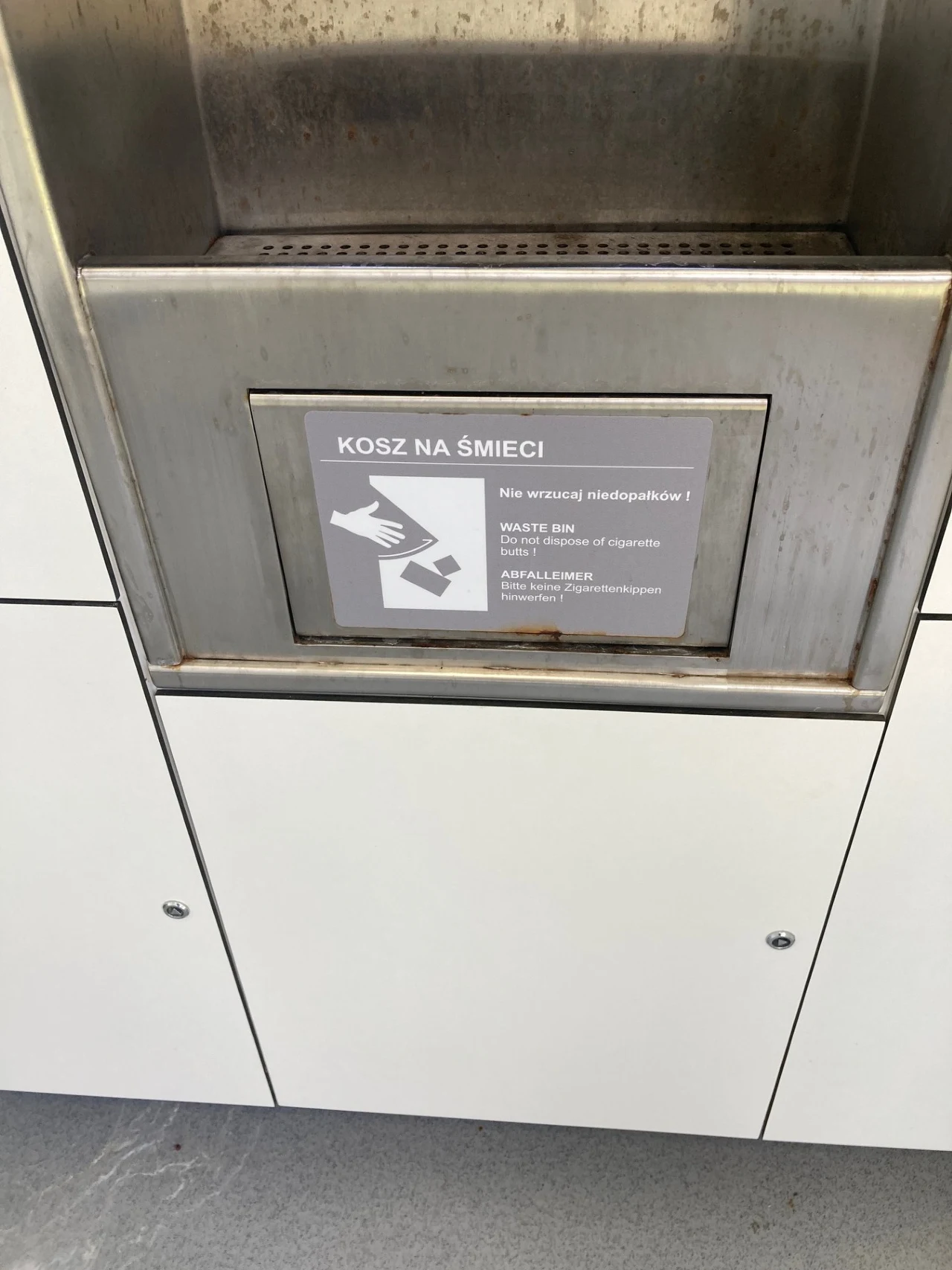 Pordzewiałe elementy zdradzają, że toaleta ma już kilka lat, z których większość stała nieużywana metalowy kosz na śmieci z napisem informacyjnym zakazującym wrzucania niedopałków oraz gum do żucia, otoczony białymi panelami