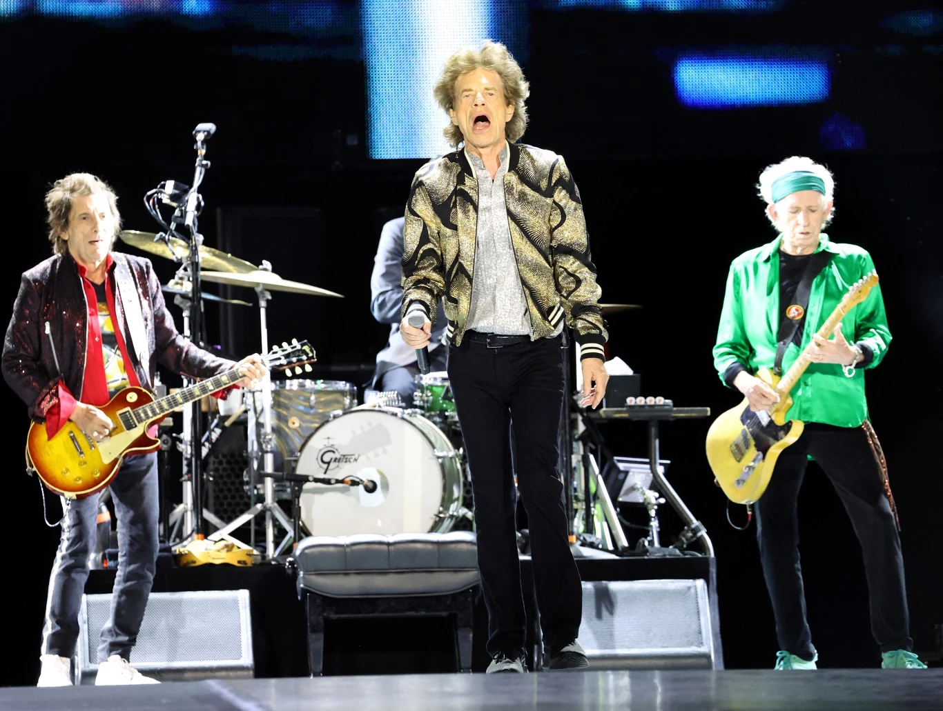 The Rolling Stones w akcji, z tyłu Ronnie Wood i Keith Richards, w środku Mick Jagger The Rolling Stones na scenie: Mick Jagger przy mikrofonie, po bokach gitarzyści, w tle perkusja i oświetlenie.